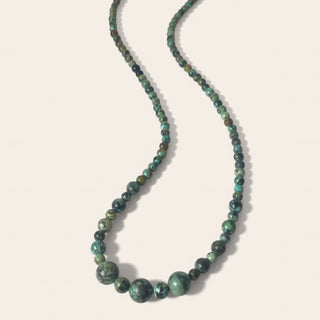 Beaded necklace with green and brown stones on a light beige background