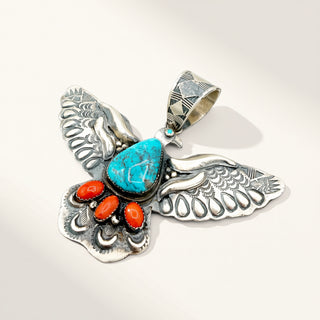 A sterling silver bird pendant featuring a large turquoise stone on the chest, four small coral stones, and a geometric patterned bail, photographed on a clean off-white background.