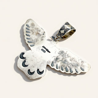 A sterling silver owl pendant with inlaid black and white stone details, shown on a light beige background.