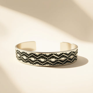 Silver cuff with designs on a beige background