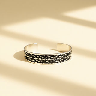 Silver cuff with designs on a beige background