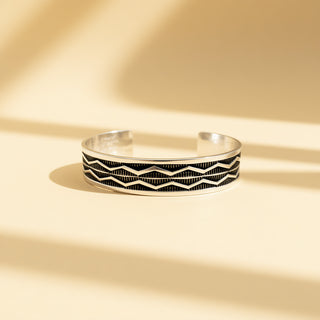 Silver cuff with designs on a beige background