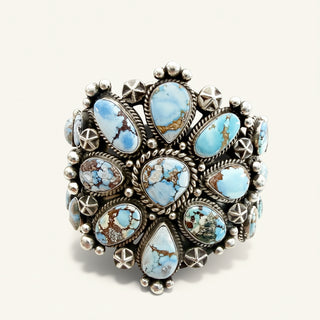 A wide sterling silver cuff bracelet featuring multiple oval and teardrop-shaped light blue turquoise stones with brown matrix, set in a Southwestern style with star and rosette motifs.
