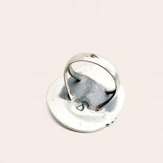 A sterling silver ring with a flat, circular disc base and a curved band that loops over the top, photographed on a solid, warm off-white background.