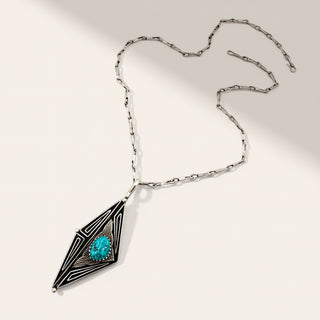 A silver geometric pendant necklace featuring a turquoise stone, displayed on a light beige background with soft shadows.