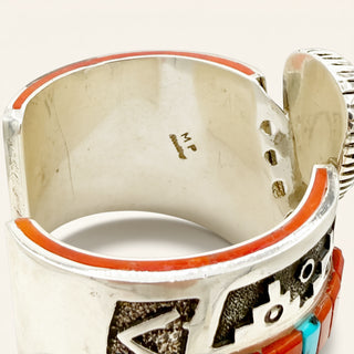 A close-up of a sterling silver cuff bracelet with hand-painted orange, black, and turquoise inlay details, showing the interior stamped with 'MP'.