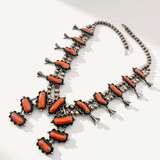A Southwestern-style silver-toned beaded necklace featuring vibrant orange coral cabochons in ornate floral settings, displayed on a clean white background.