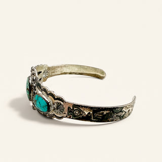 A sterling silver cuff bracelet featuring turquoise stone accents and hand-painted floral details, shown on a light cream background.