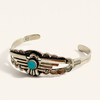 A silver-toned Southwestern-style cuff bracelet featuring a central turquoise stone and sunburst details, photographed on a clean off-white background.