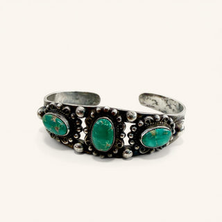A silver cuff bracelet featuring three oval green turquoise stones in ornate silver settings, photographed on a clean off-white background.