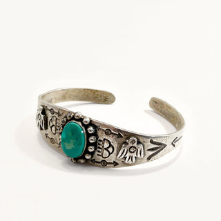 A silver cuff bracelet featuring a central oval green turquoise stone and hand-stamped Native American style symbols, photographed on a clean white background.