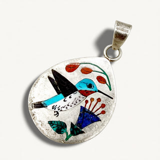 A teardrop-shaped silver pendant featuring colorful inlay artwork of a hummingbird, flowers, and leaves on a light background.