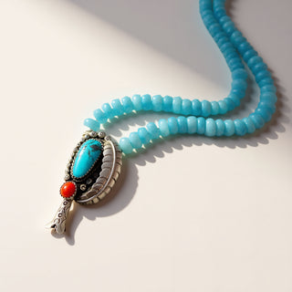 Turquoise beaded necklace with a silver pendant featuring a blue stone and red gem on a light background