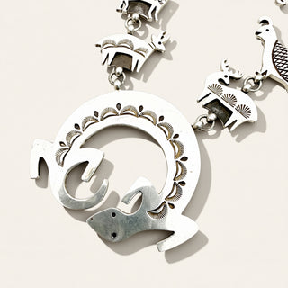 A close-up of a silver-toned jewelry piece featuring a large circular pendant with stylized animal motifs  on a light beige background.
