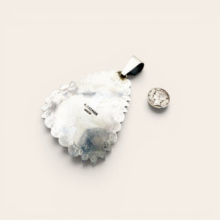 Jewelry pendant, back silver, with a stamp saying "A. Cadman"  on a light background