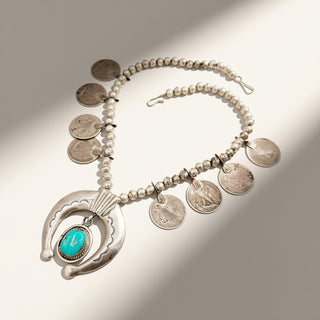 silver necklace on a beige background with coin pendants and a turquoise stone center 