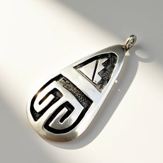 A silver teardrop pendant with a Southwestern-style geometric design, featuring oxidized black recesses, photographed on a white surface with a soft shadow.
