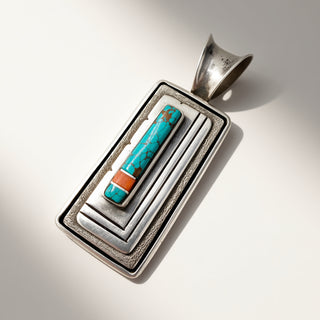 Silver pendant with turquoise and coral inlay on a light gray background