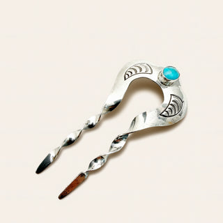 A sterling silver hair claw clip with engraved geometric patterns and a small round turquoise stone accent, shown on a solid light beige background.
