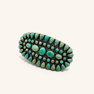 A wide silver-toned jewelry embellished with multiple rows of green turquoise stones in various teardrop and oval shapes, set against a plain off-white background.