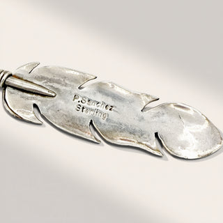 Silver feather-shaped pendant with 'P. Sanchez Sterling' engraving on a light gray background
