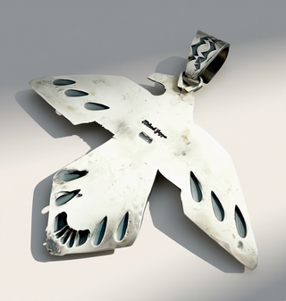 The back of a silver bird pendant showing the name Richard Yazza on a cream background