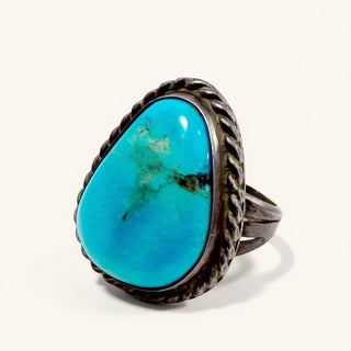 A sterling silver ring featuring a large, teardrop-shaped turquoise cabochon with natural matrix patterns, set against a clean off-white background.