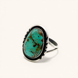 A sterling silver ring featuring a large, irregularly shaped turquoise stone with natural brown matrix patterns, set in a bezel-style oval frame on a plain off-white background.