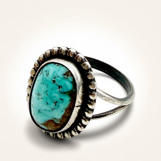A sterling silver ring featuring a large, oval-shaped turquoise stone with natural brown matrix details, set in a textured bezel with a beaded border.