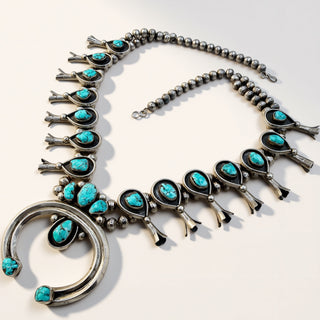 A silver-toned Southwestern-style necklace featuring multiple turquoise cabochon stones set in black bezel settings, with a large curved cuff section and a beaded chain closure, displayed on a light neutral background.