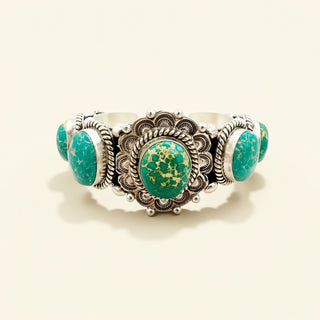 Silver cuff with green stones on a beige background