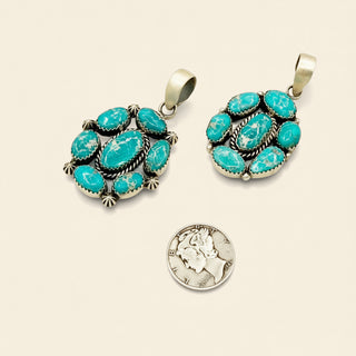 Two turquoise stone pendants on silver chains with a coin on a beige background