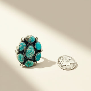 Turquoise ring with silver accents next to a quarter on a beige background