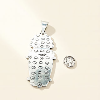 Silver pendant with engraved design on a beige background